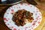 A white plate dotted with red painted snowflakes, with a helping of Red Kettle Maine Kelp kimchi in the center, placed on a rustic wood cutting board. The kelp is prominently placed on top with small pieces of napa cabbage and gochugaru red pepper flakes visible underneath.