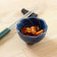 A small blue bowl in the shape of a flower, holding a serving of kimchi