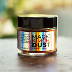 A jar of Red Kettle Magic Kimchi Dust Seasoning with a holographic label displaying the product name and description, set on a table with a blurred background.