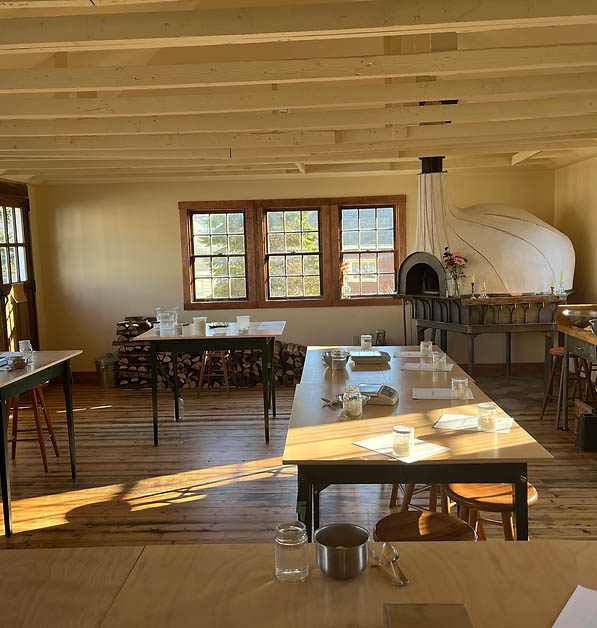 The inside of the restaurant and class space at the Uproot Pie Co in Thomaston, with a wood fired pizza oven in the corner and warm sunlight streaming through the windows.