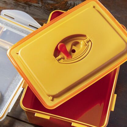 A kimchi fermentation box is open on a wooden table, showing the two lids used: one with a silicon gasket and a second clear top lid.