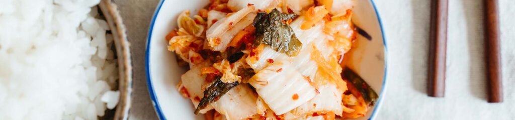 A small porcelain dish filled with kimchi, centered between wooden chopsticks and a bowl of rice.