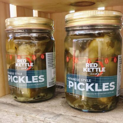 Two jars of pickles in a wooden crate displayed for a market